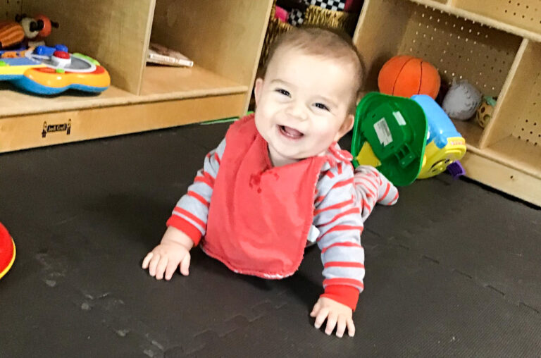 Baby smiling and crawling on a mat.