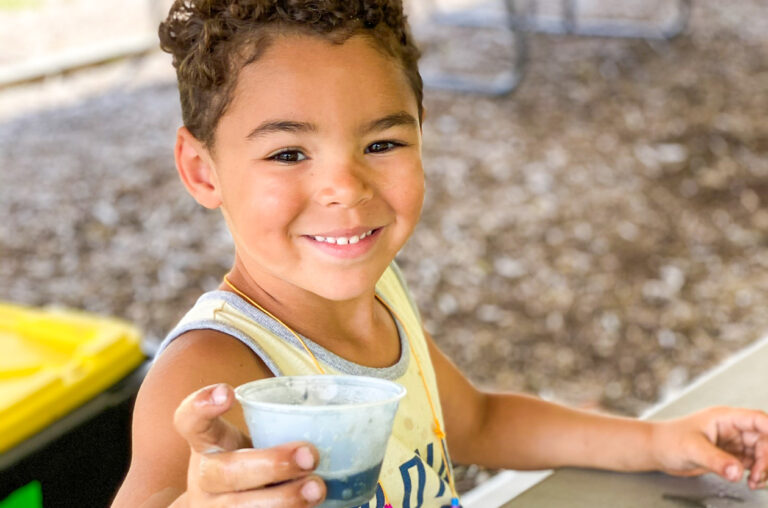 A boy smiling holding a cup.