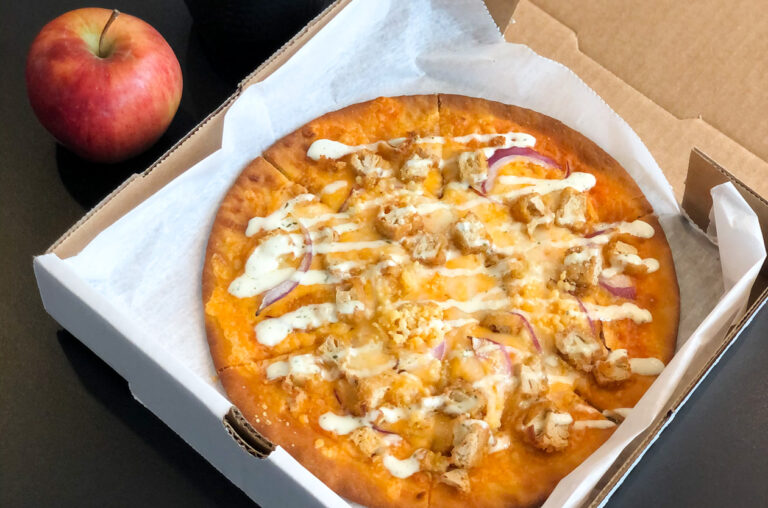 A fresh buffalo chicken pizza and a red apple.