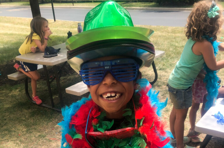 A boy smiling and wearing a feather boa and funny sunglasses.