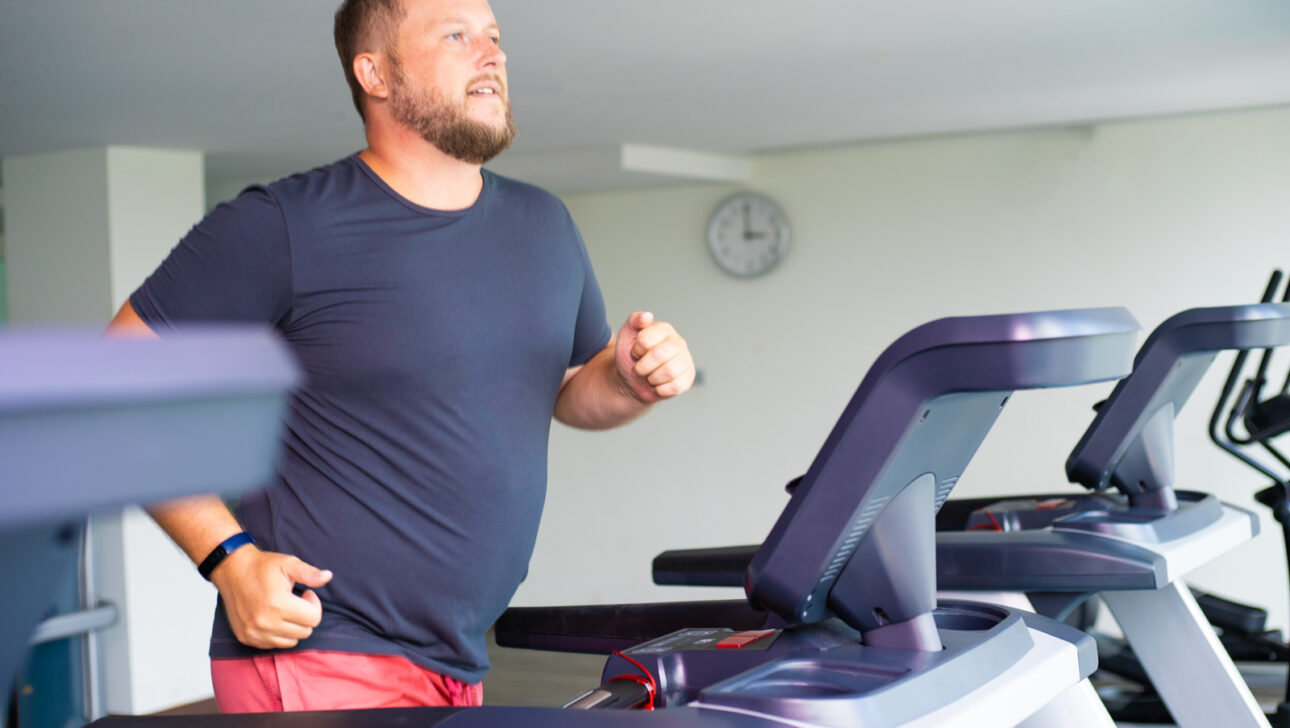 chubby man walking on running track, warming up on gym treadmill.
