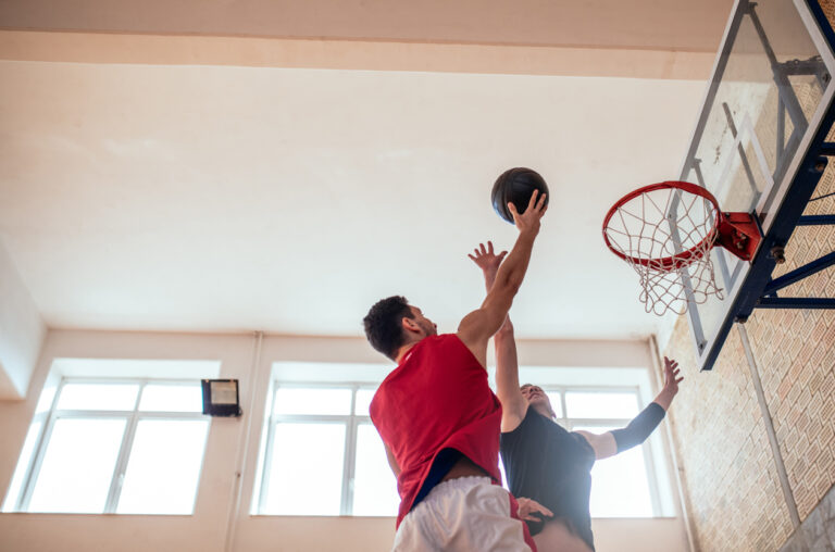 Two young man playing basketball indoors.