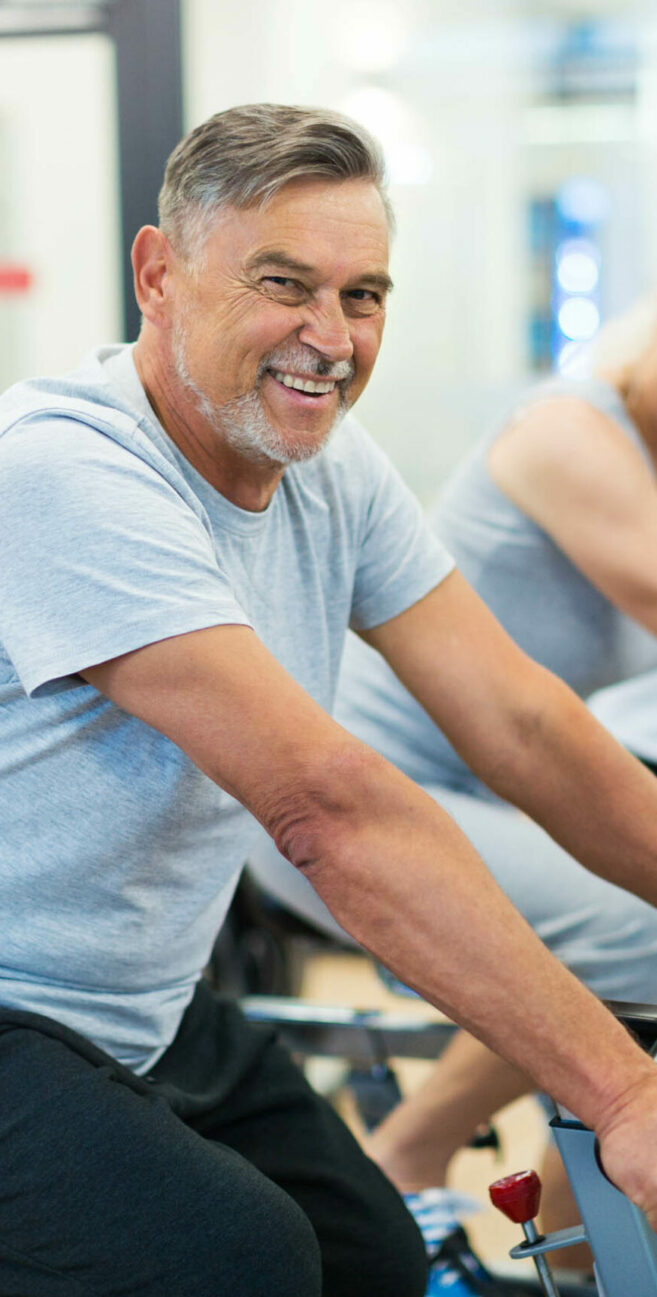 Confident seniors on exercise bikes in spinning class at gym.