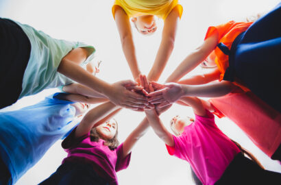 Kids putting their hands together indoors in rainbow t-shirts