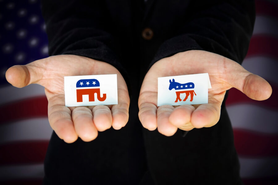 man holds in his hands Elephant symbol of the Republican Party and the Donkey symbol of the Democratic Party, with the American flag behind. concept of elections from the United States of America