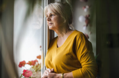 Woman wearing a yellow shirt and staring out a window sadly