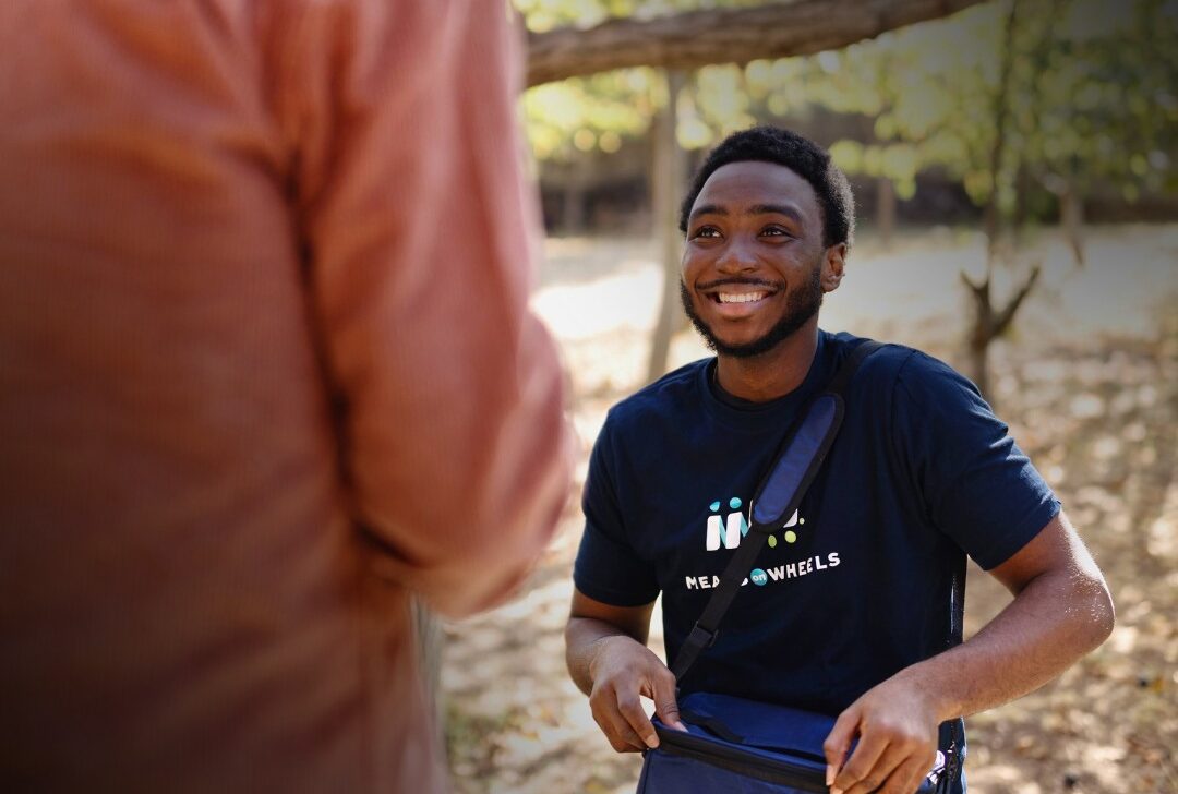 Share the love event. Person visiting an elderly man with meals on Wheels food.